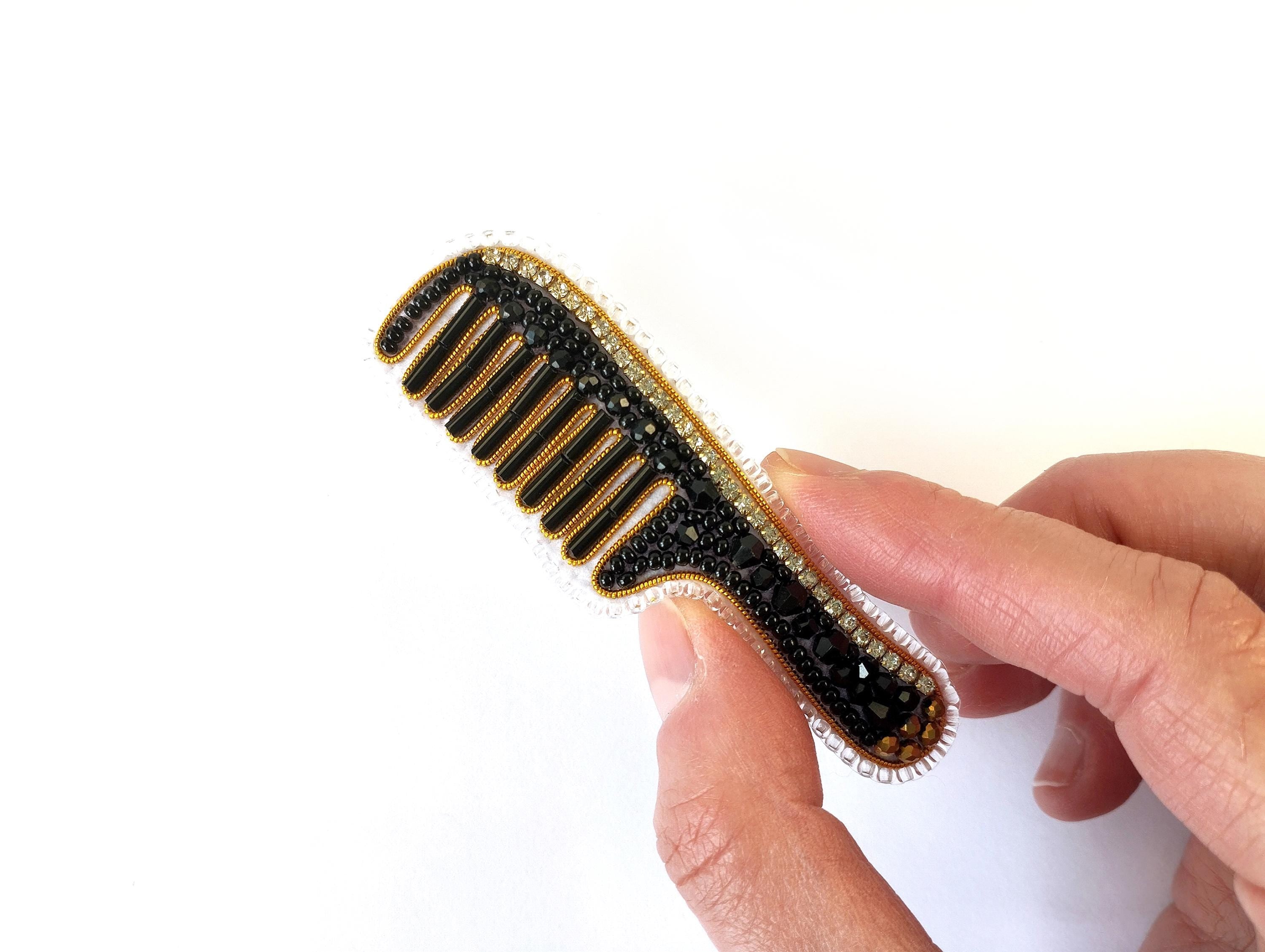 A hand holding a black and gold comb with rhinestones or crystals on it.